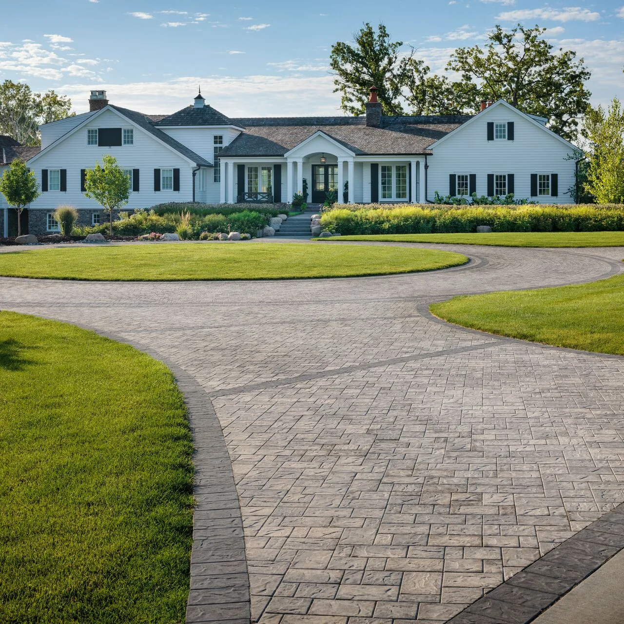 A generous arrival Broad paver driveway curving through lawns in front of a large white house.