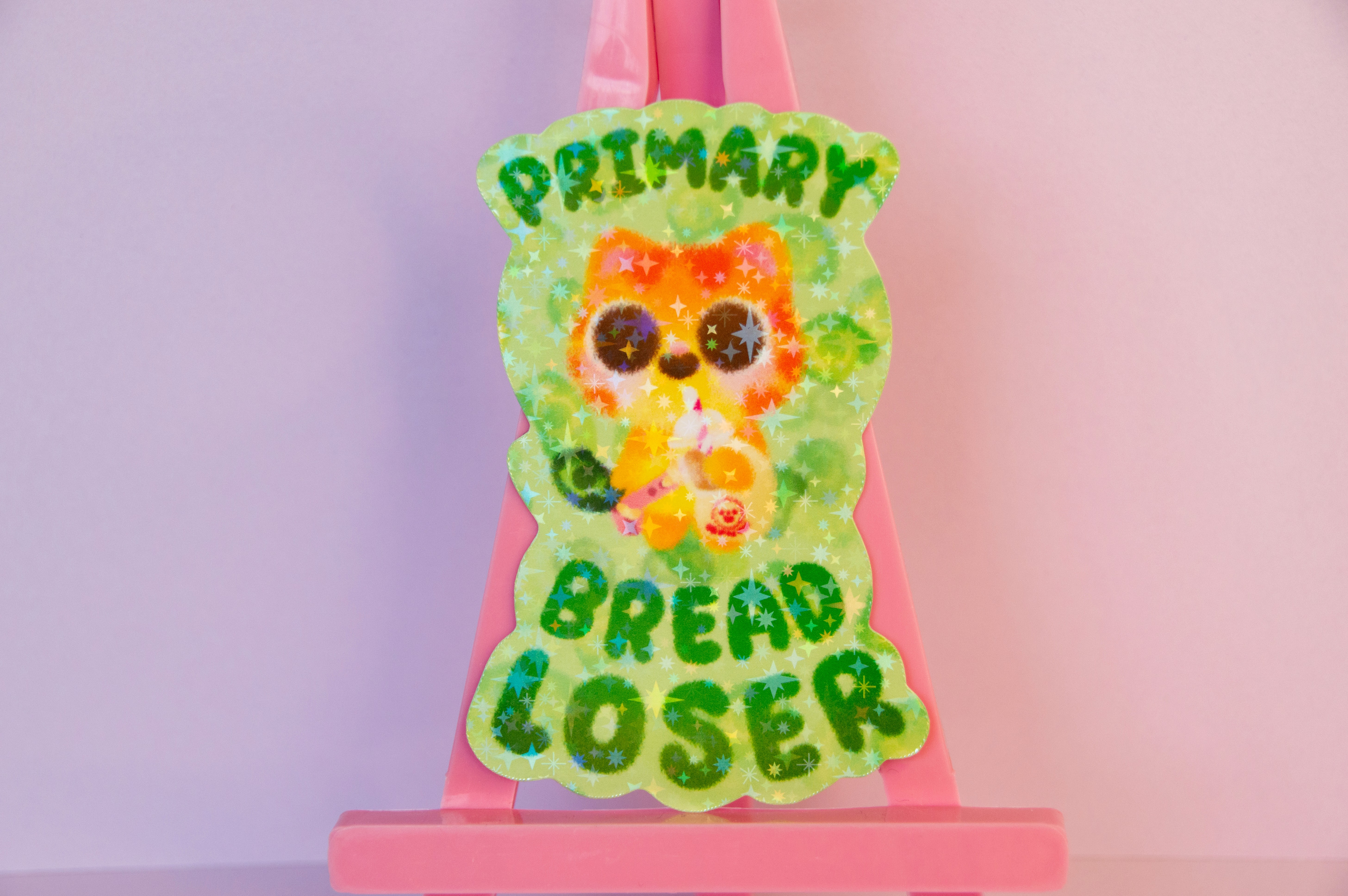 A green, sparkly sticker of an orange cat, carrying a bag, a drink, and a banknote. It reads "Primary bread loser".
