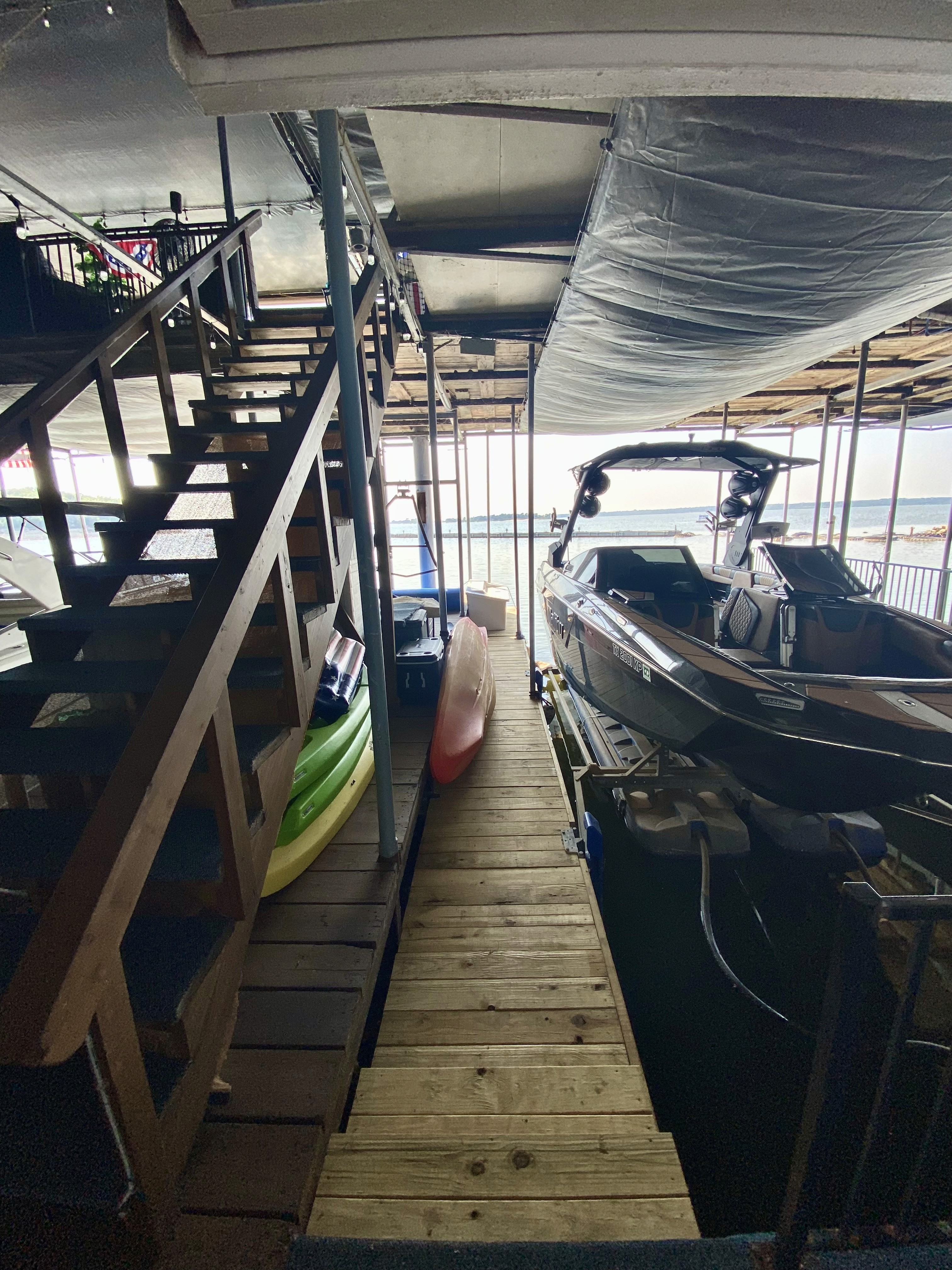 Wooden dock with boats, kayaks, and stairs. Boat is parked on the dock and the other two boats are kayaks. 