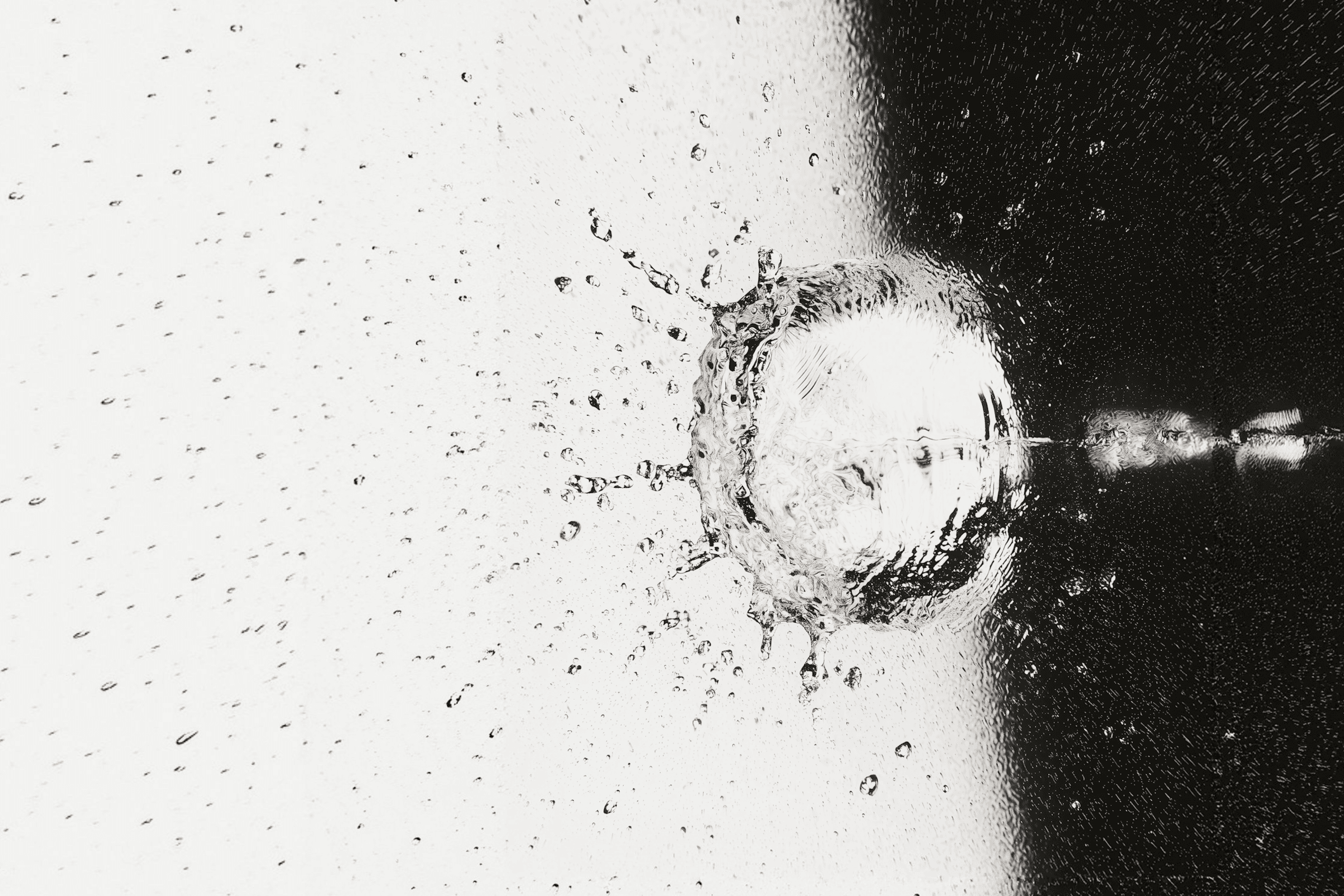 Monochrome high-speed shot of a water droplet impact, showcasing a dramatic splash with intricate details and contrasting light and dark tones.