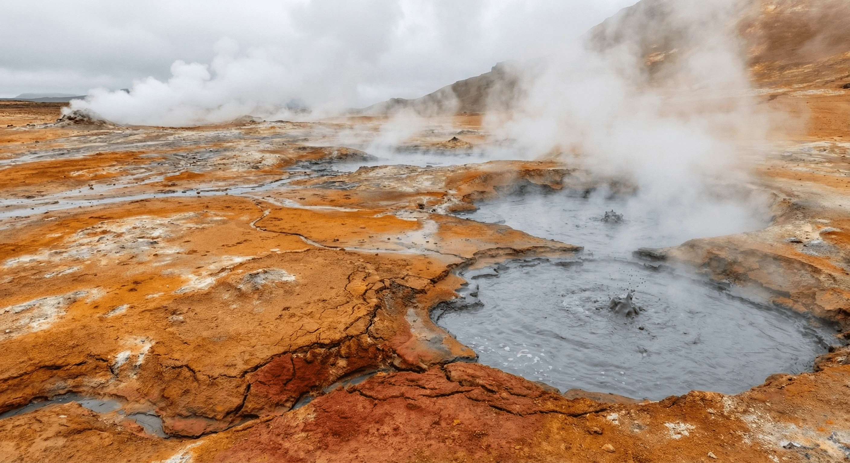 A geothermal area featuring bubbling mud pots and steam rising from colorful red and orange clay ground.