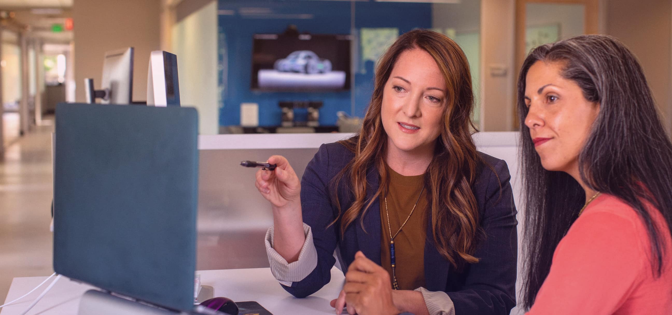 Two women engaged in a serious discussion in an office setting, with one holding a pen and explaining something to the other.