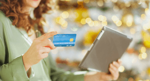 A woman holds a credit card in one hand and a tablet in the other.