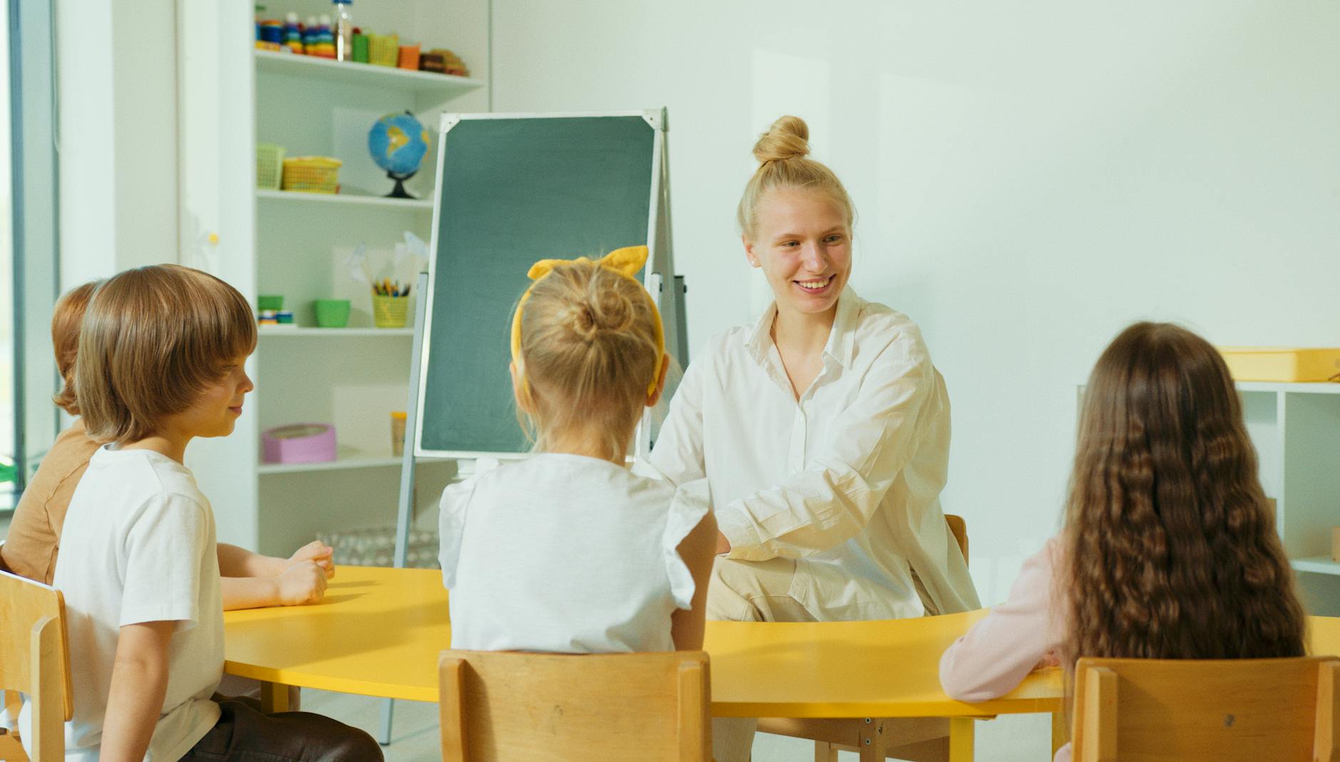 A teacher standing at a whiteboard pointing to text while students laugh during an interactive read-aloud.