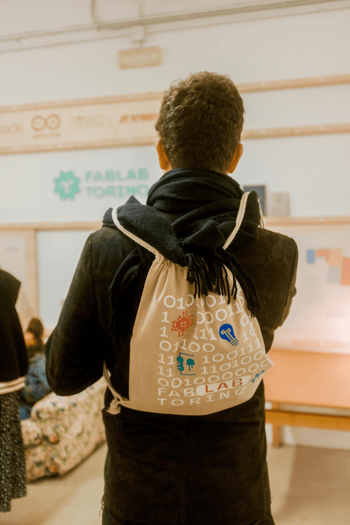 The photo of a person portrayed from the back. The person holds a backpack customized with the event graphics.