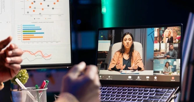 Tela de laptop mostrando uma videochamada com vários participantes, ao lado de um gráfico projetado