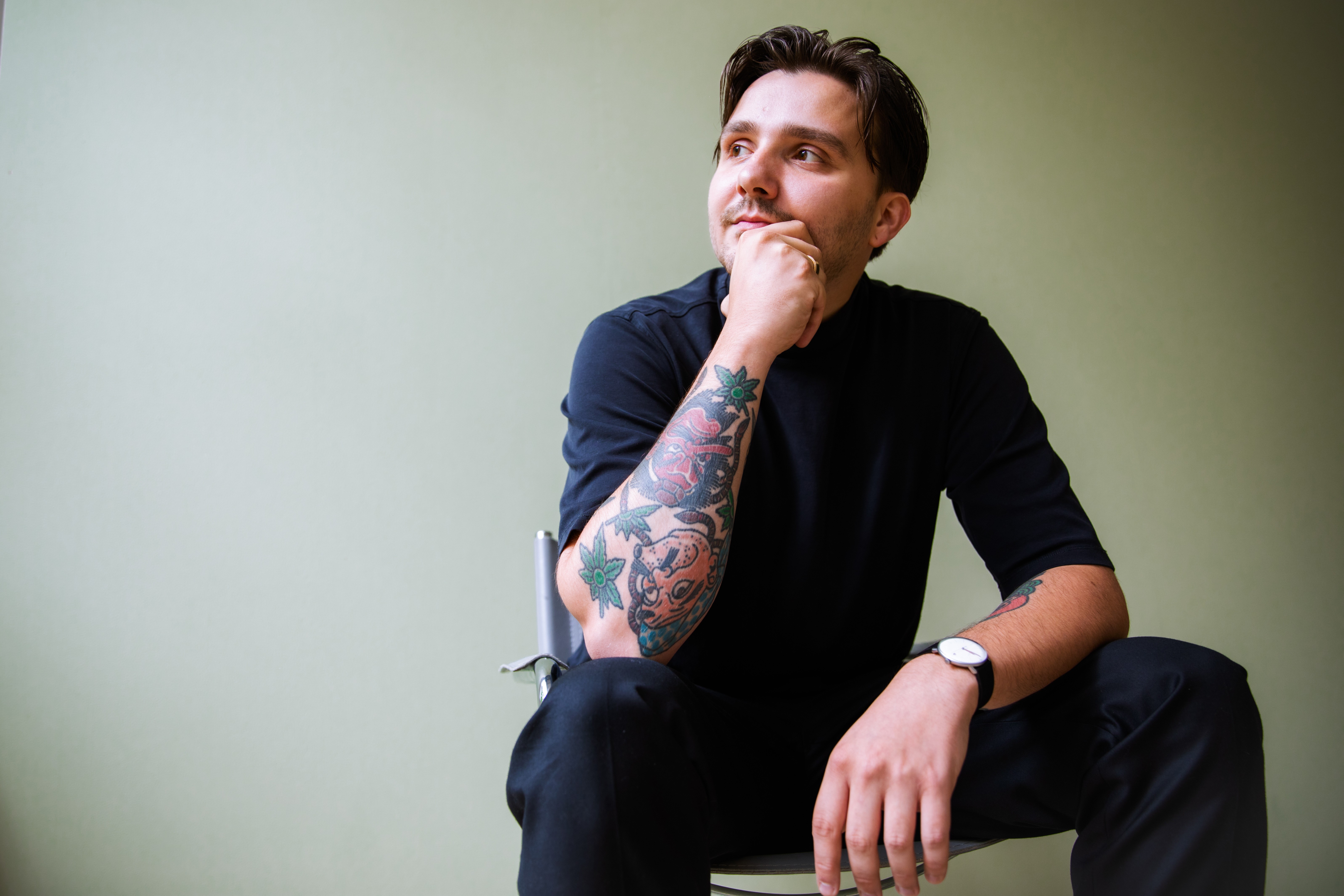 mann mit schwarzer kleidung sitzt vor einem grünen hintergrund und schaut nach links