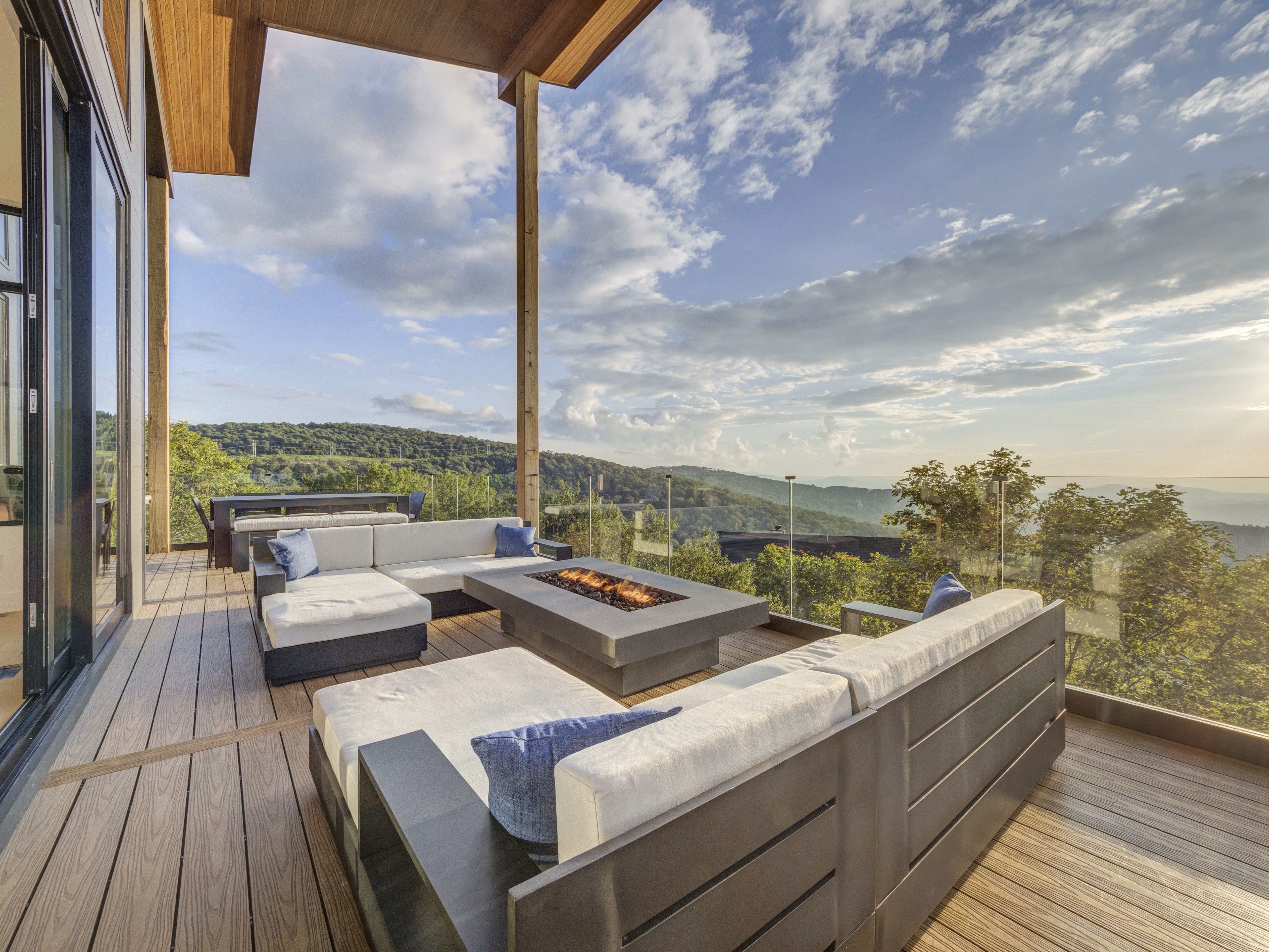 Wide-angle shot of a grey outdoor sectional sofa and a concrete fire pit on a luxury deck during golden hour
