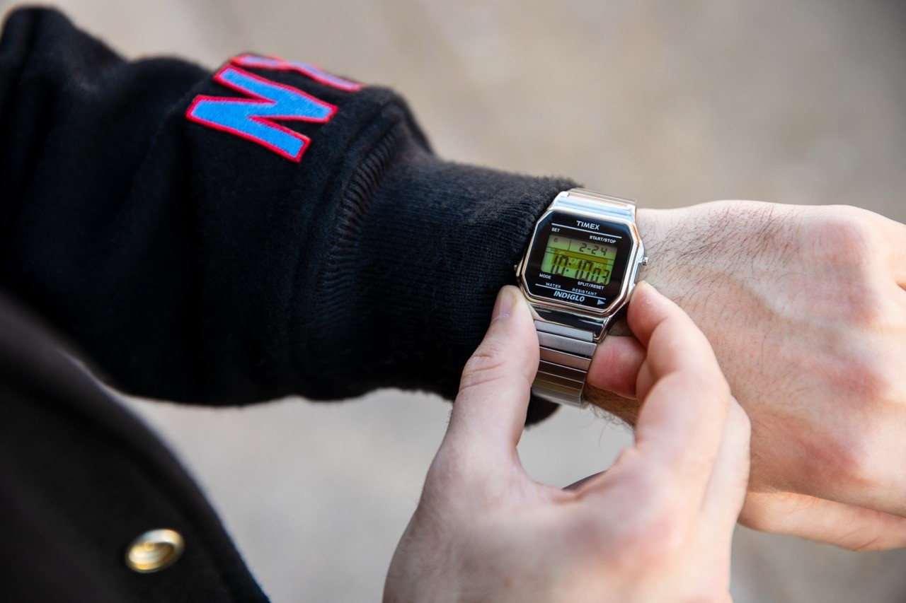 Close-up of a hand adjusting a metal digital wristwatch on the wrist.