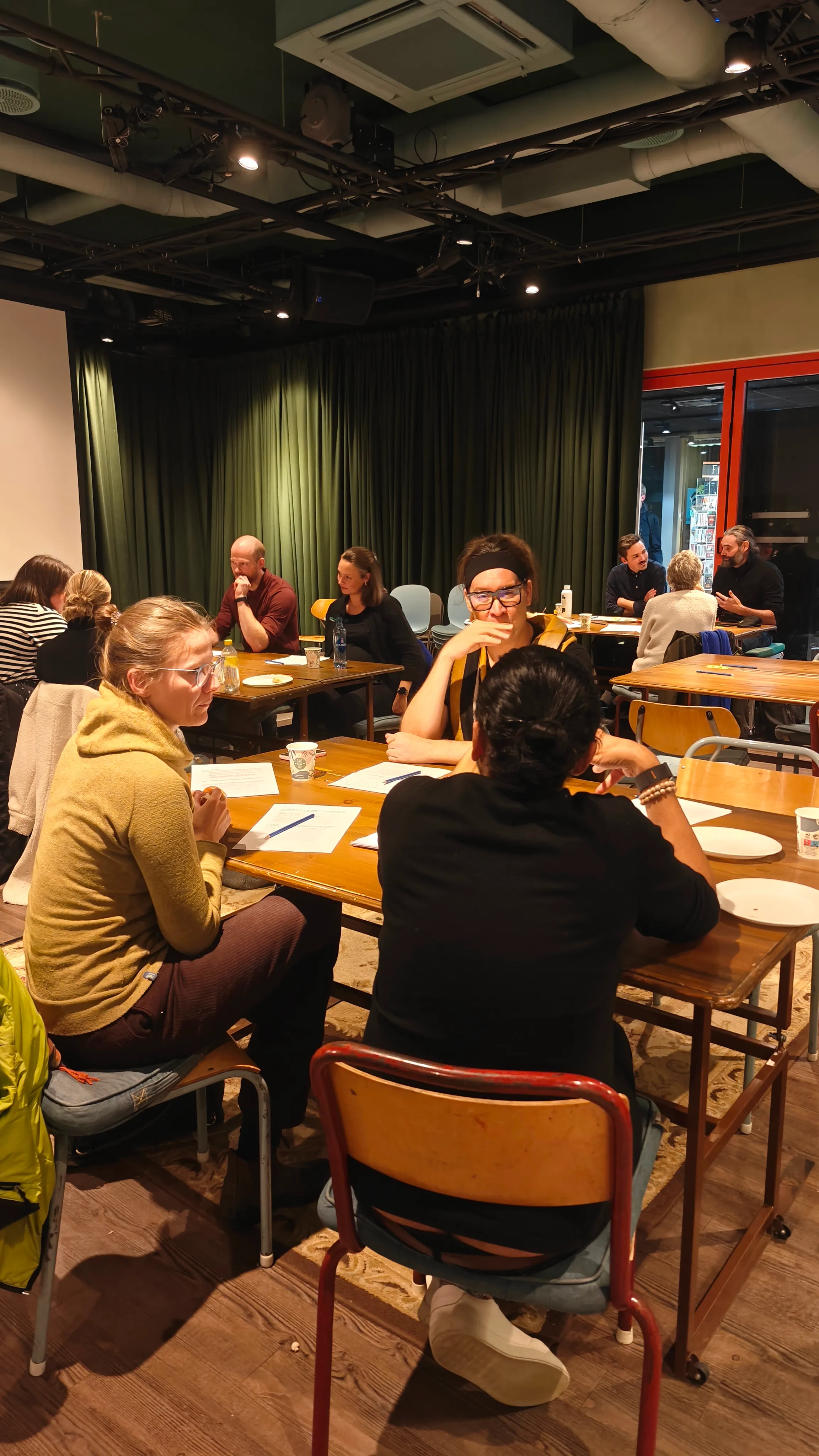 Several groups of people sitting down and talking around tables in a room