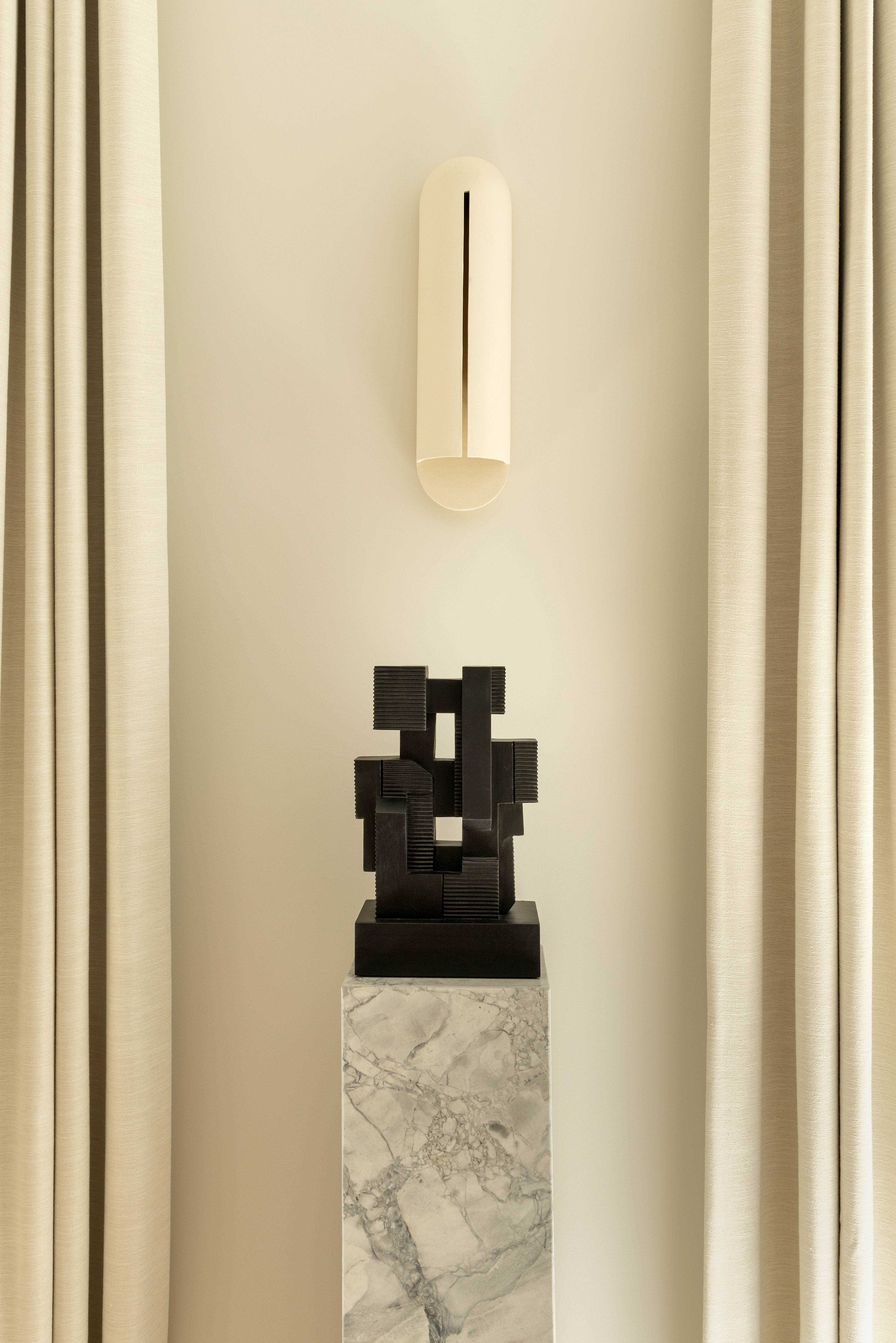 Sculpture contemporaine noire sur socle en marbre gris, applique murale minimaliste et rideaux beiges