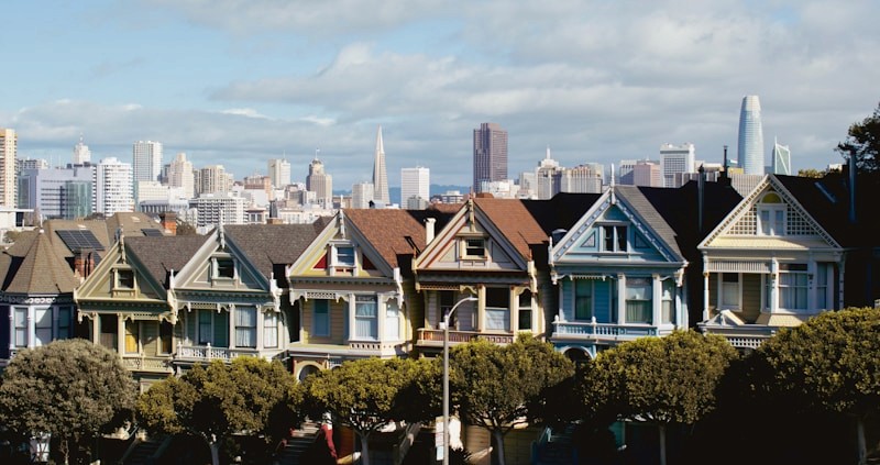 Row of colorful Victorian houses with a city skyline at dusk