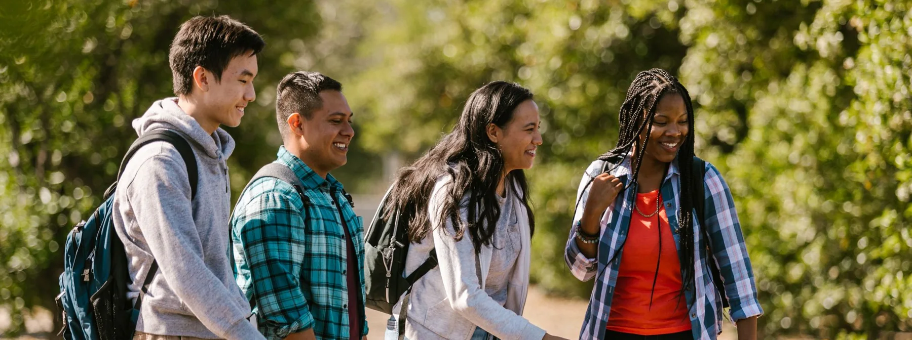 Four high school students laughing together outdoors with backpacks