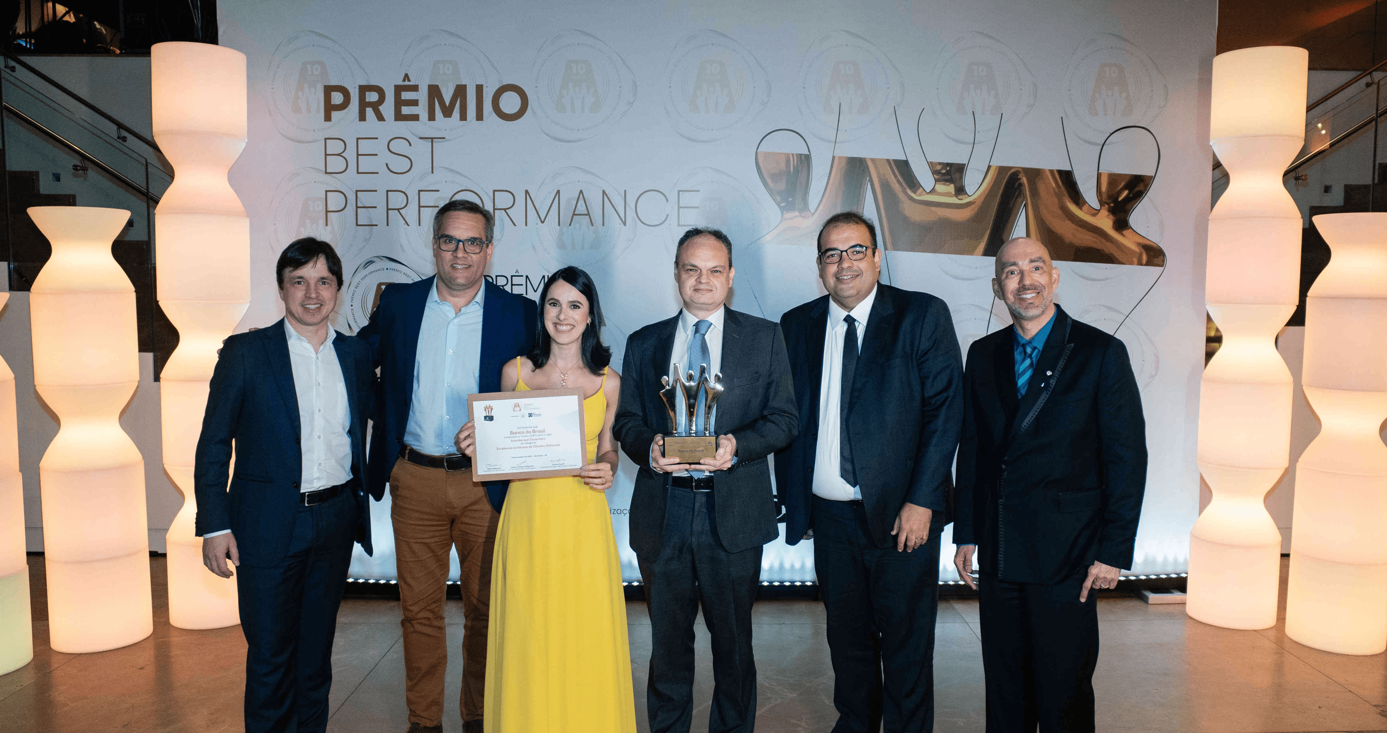 Executivos do Banco do Brasil posando com troféu ouro e certificado no palco do Prêmio Best Performance 2025