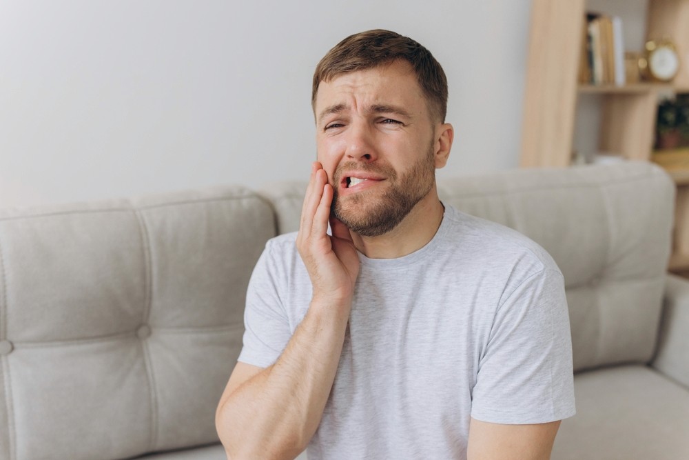 A man experiencing jaw pain due to Temporomandibular Joint Disorder, holding his jaw in discomfort
