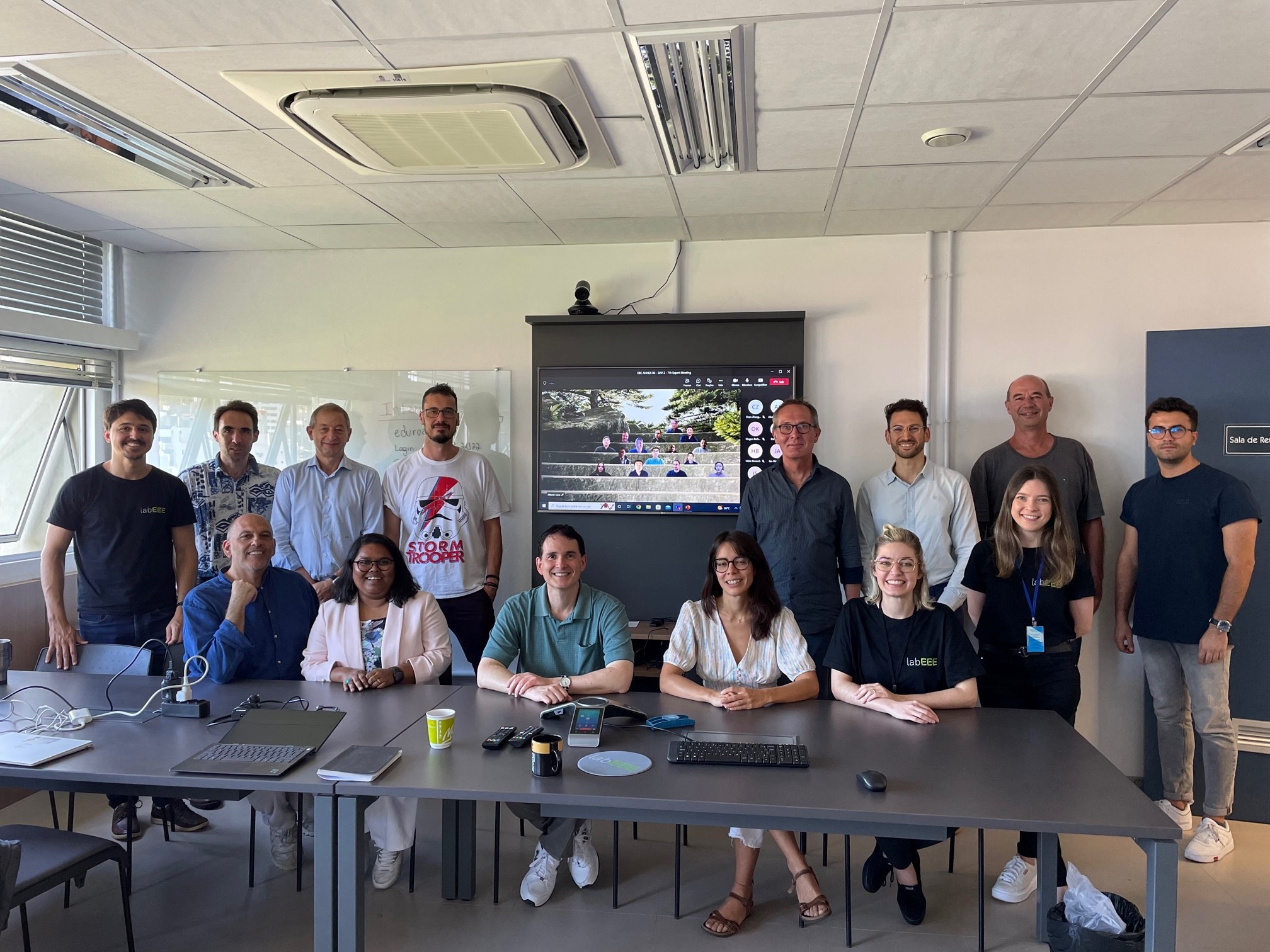 A group of people smiling and posing for a photo in front of a large digital screen displaying colorful graphics.