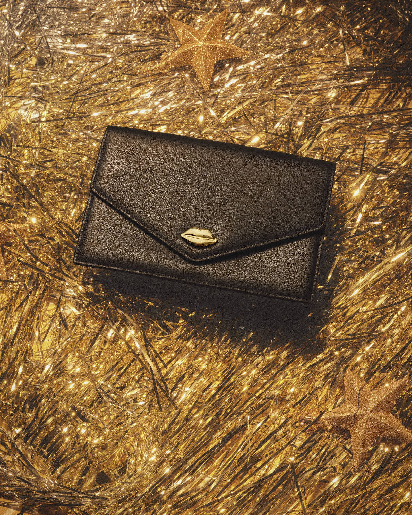 Elegant black clutch with gold accent on sparkling gold background.