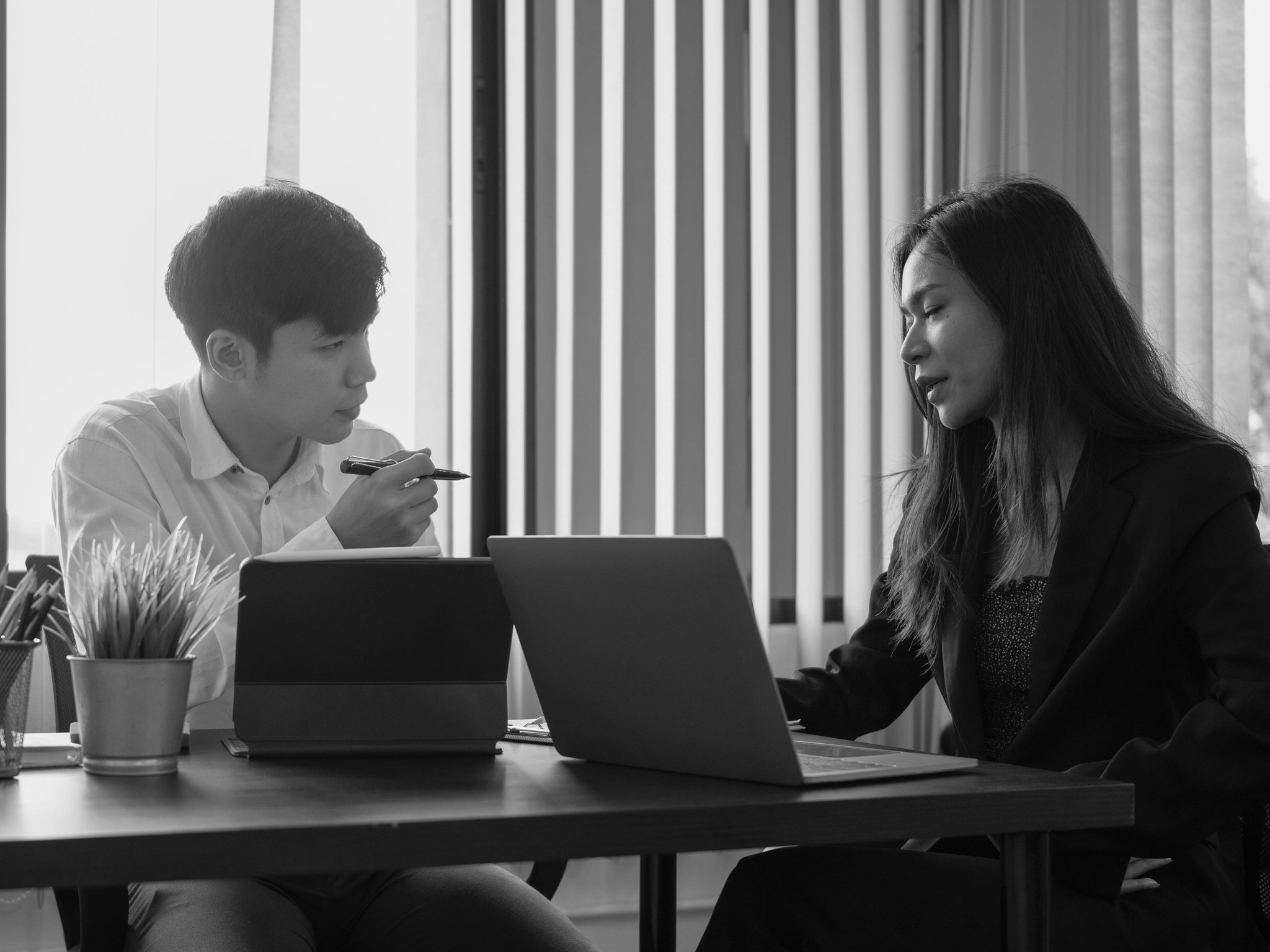 Black and white photo of two people looking at a computer screen with papers on wall