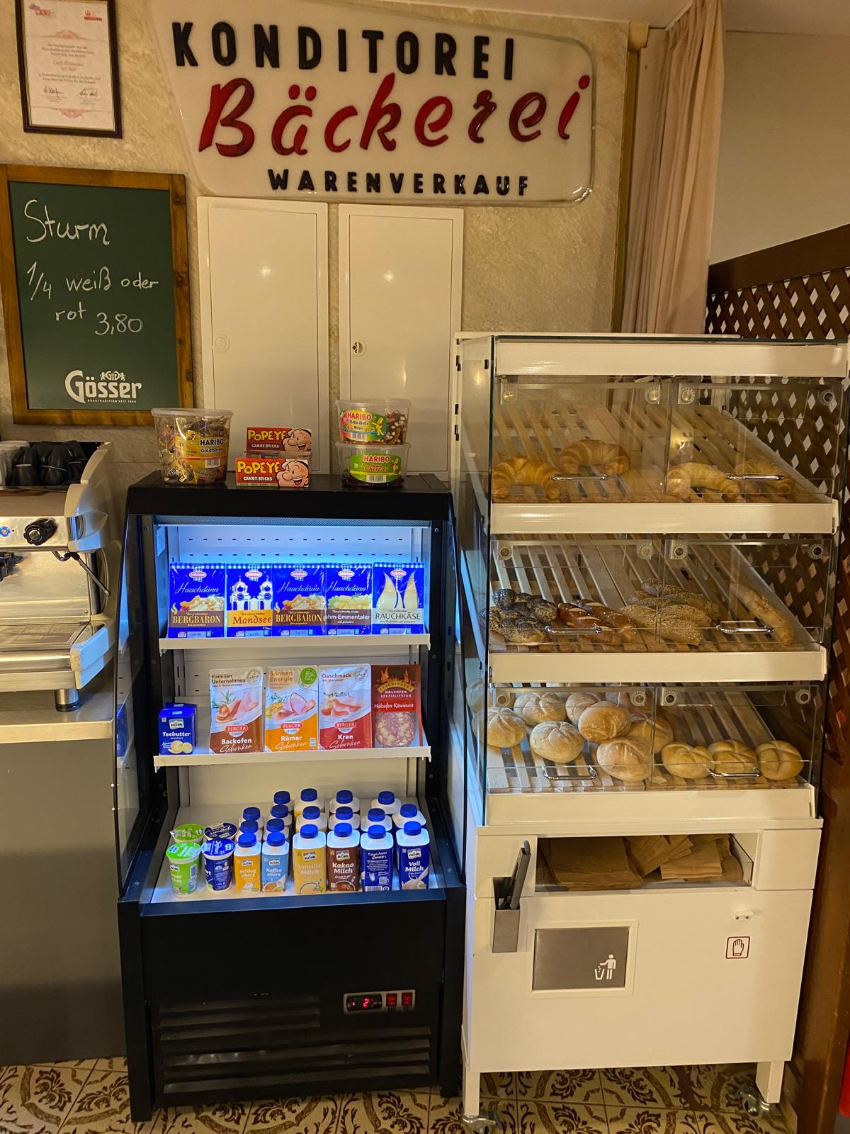 Person with a mustache wearing a black t-shirt carrying a tall stack of pizza boxes inside a dimly lit bar or restaurant.