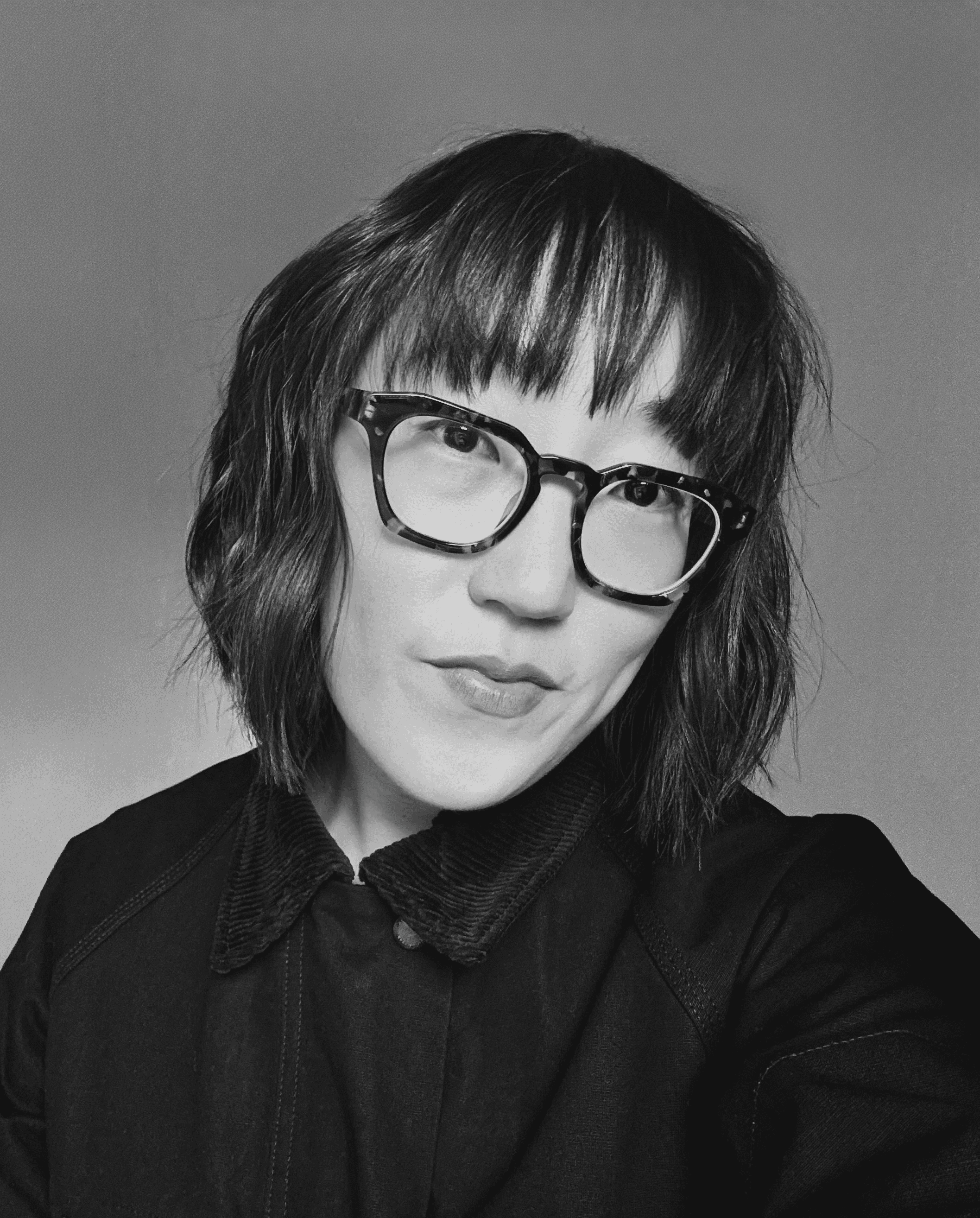 Sojin Rank, a Korean woman with short brown hair and bangs wearing large-framed glasses and a black jacket.