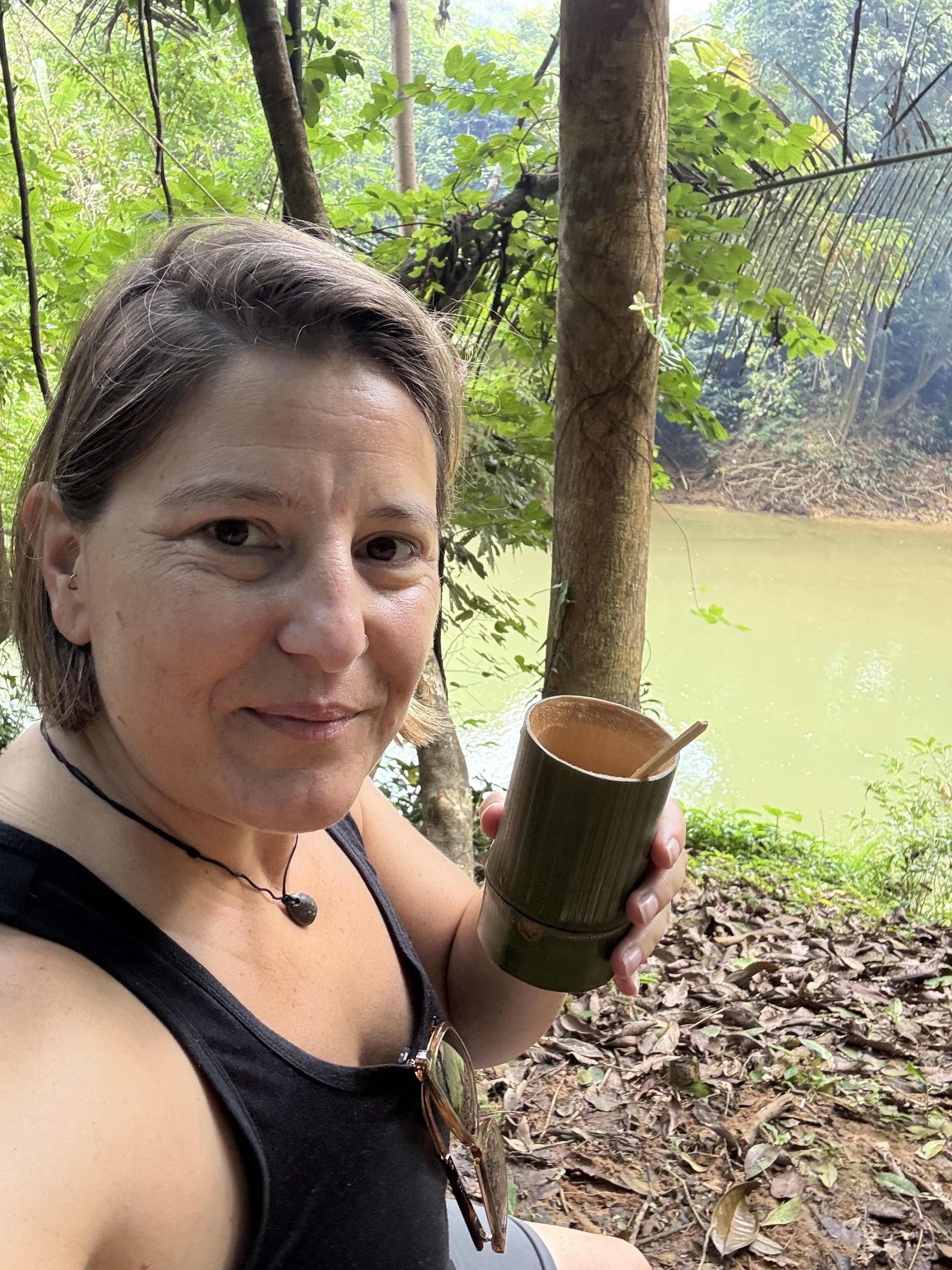 Aylin enjoying coffee from a bamboo cup beside a river