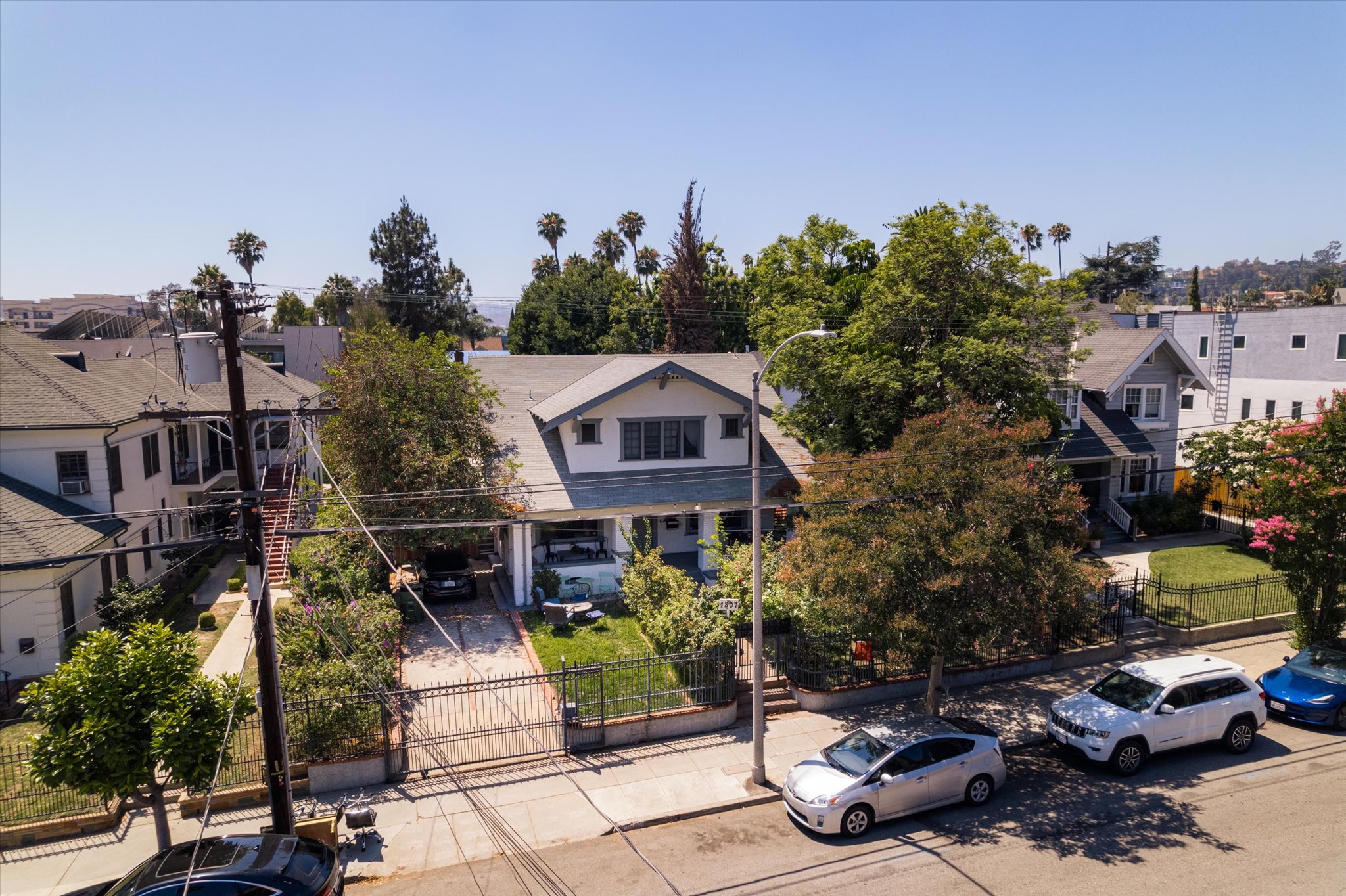 Aerial view of a neighborhood around 1807 n van ness, featuring houses, trees, and parked cars under a clear blue sky.