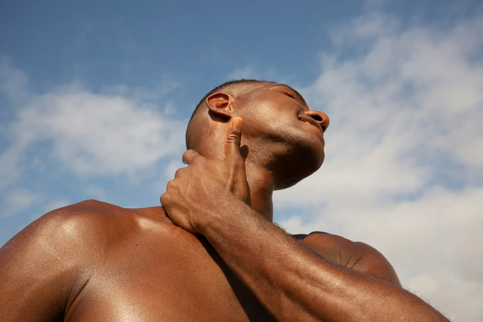 Muscular man with bronze-tanned skin flexing against blue sky, demonstrating results from tanning salon services.