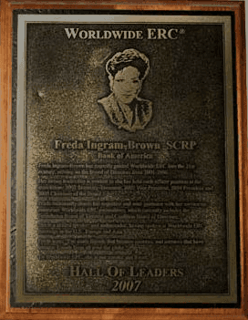 A bronze plaque featuring a portrait and text, mounted on a wooden background.