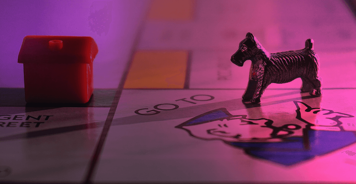 (photo by suzie hazelwood) a dog on a momopoly board looking at a house they can't afford