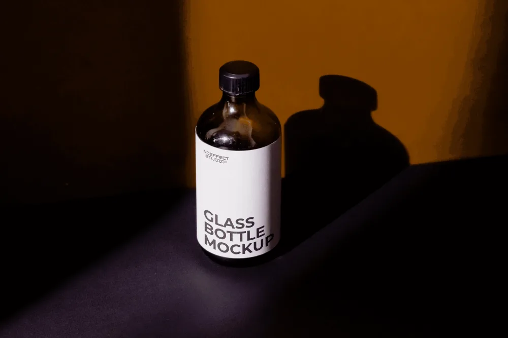 Mockup of a dark amber glass bottle with a black cap and a minimalist white label, placed on a dark surface. The scene features dramatic lighting, casting bold shadows on a warm mustard backdrop.