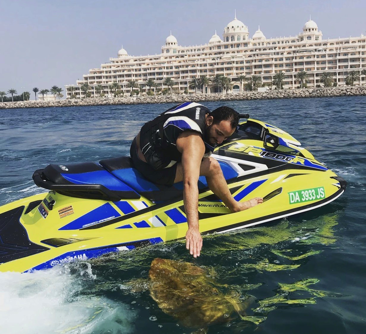A person riding a jet ski is leaning toward the water to touch it.