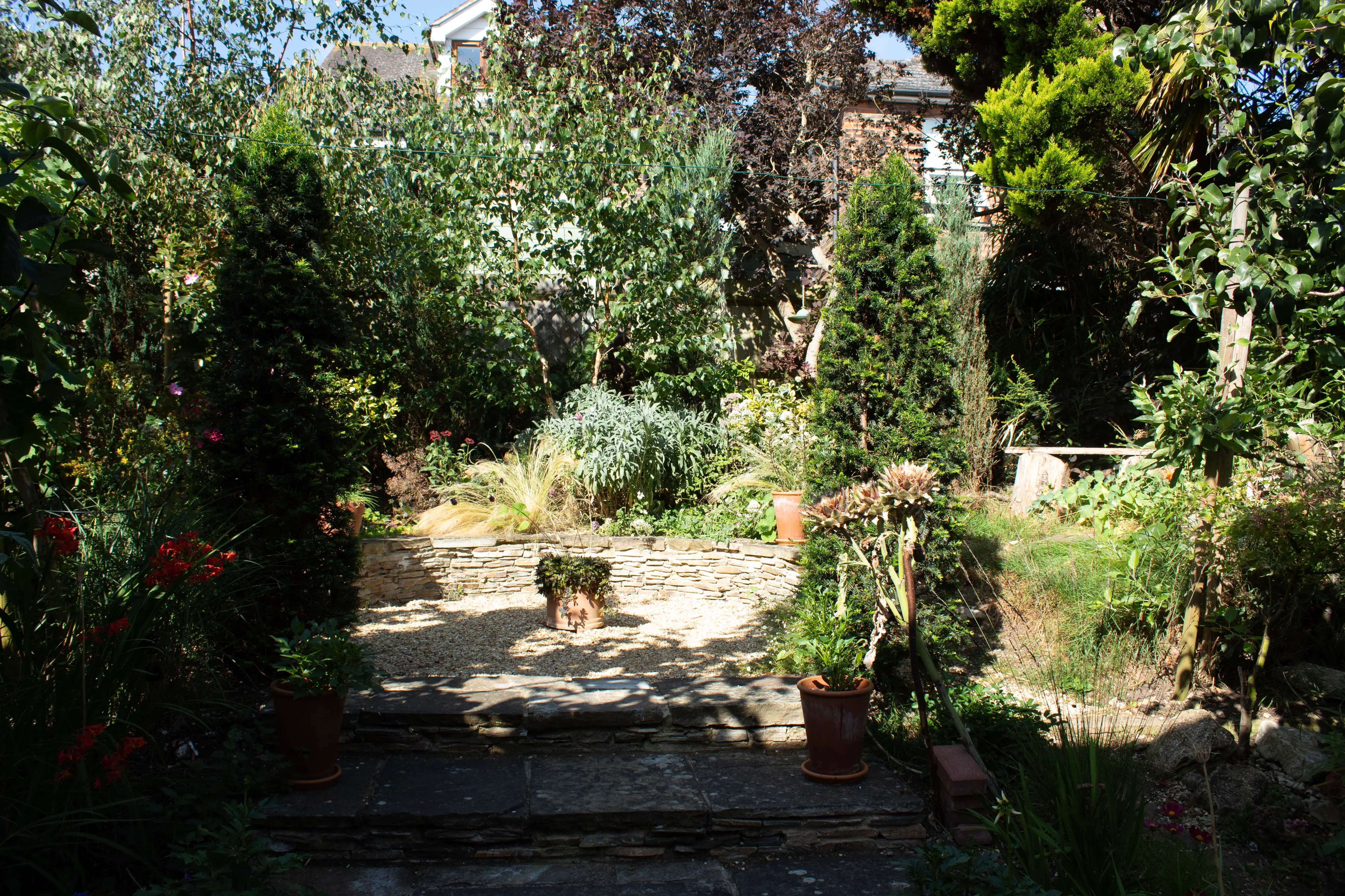 A serene garden scene featuring lush greenery, blooming flowers, and a stone pathway under a bright sky.