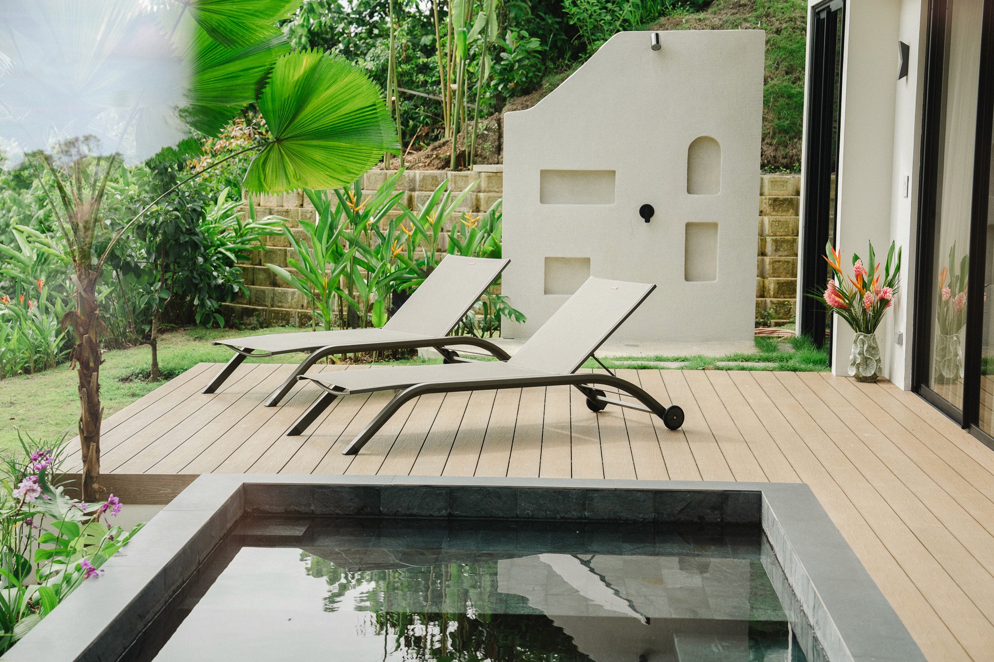 Private plunge pool and wooden sun deck with modern lounge chairs and a unique outdoor shower feature surrounded by tropical foliage.