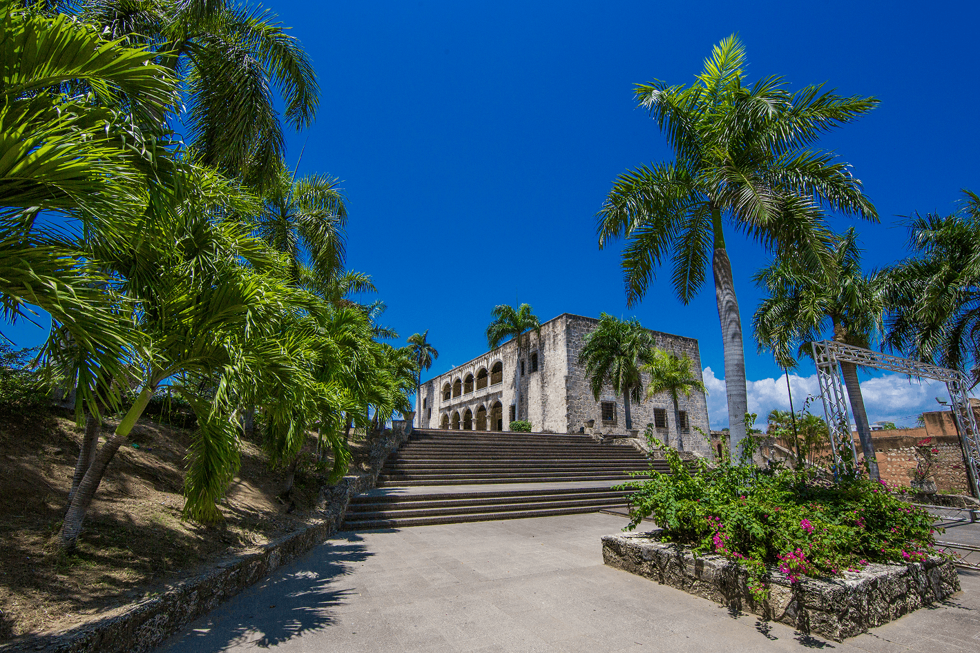 Colonial stone palace with arched loggia, broad steps, and tall palm trees.
