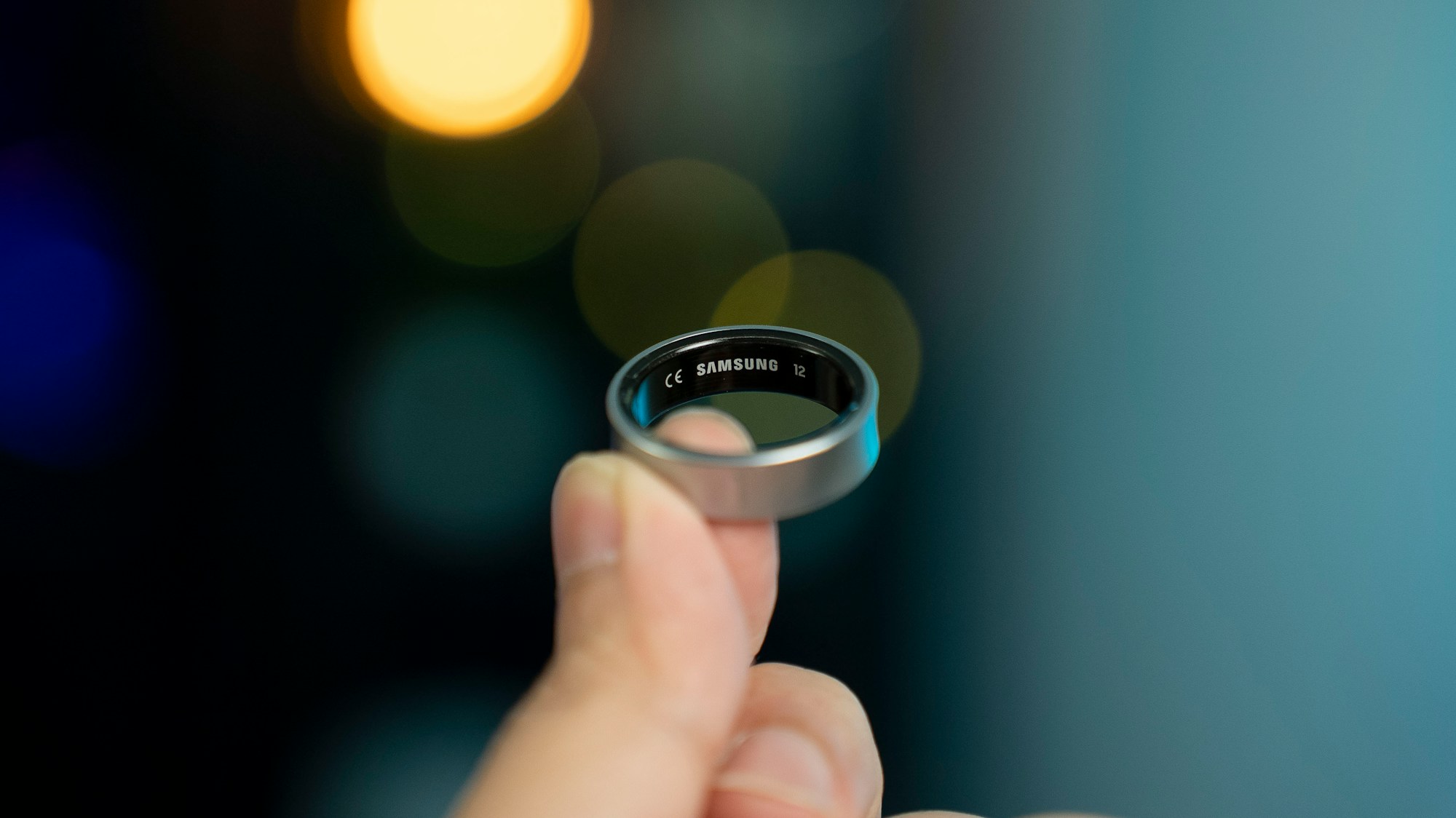 Eine Hand hält einen dunklen Smart Ring vor blauem Hintergrund