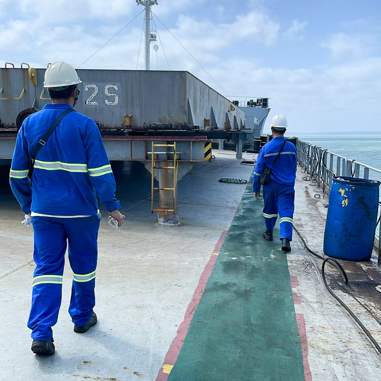 Two marine surveyors in PPE on a bulk carrier at Itaqui Port anchorage, mobilizing to inspect seven cargo holds.