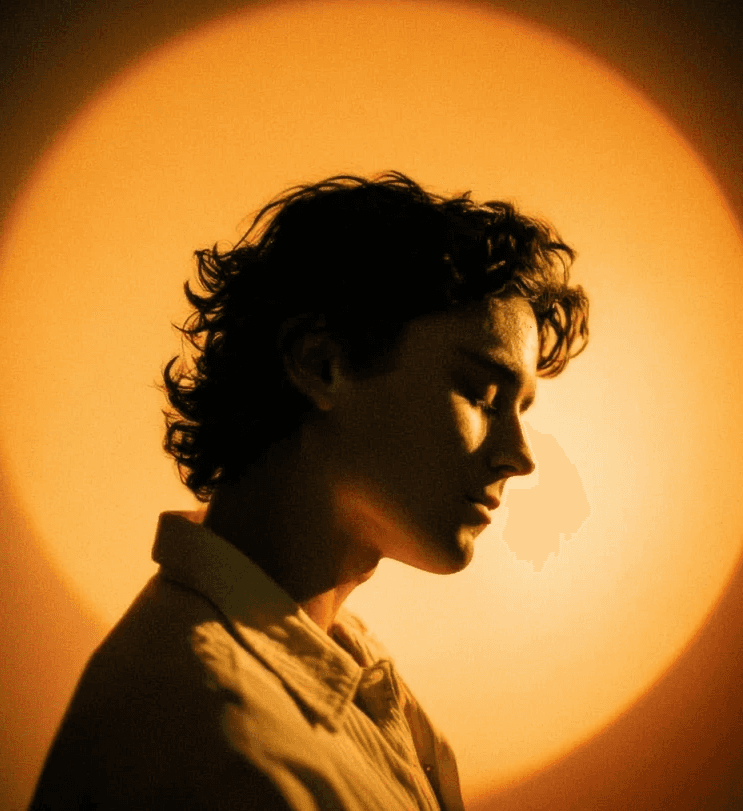 Warm cinematic side-profile portrait of a young man with glowing circular backlight.