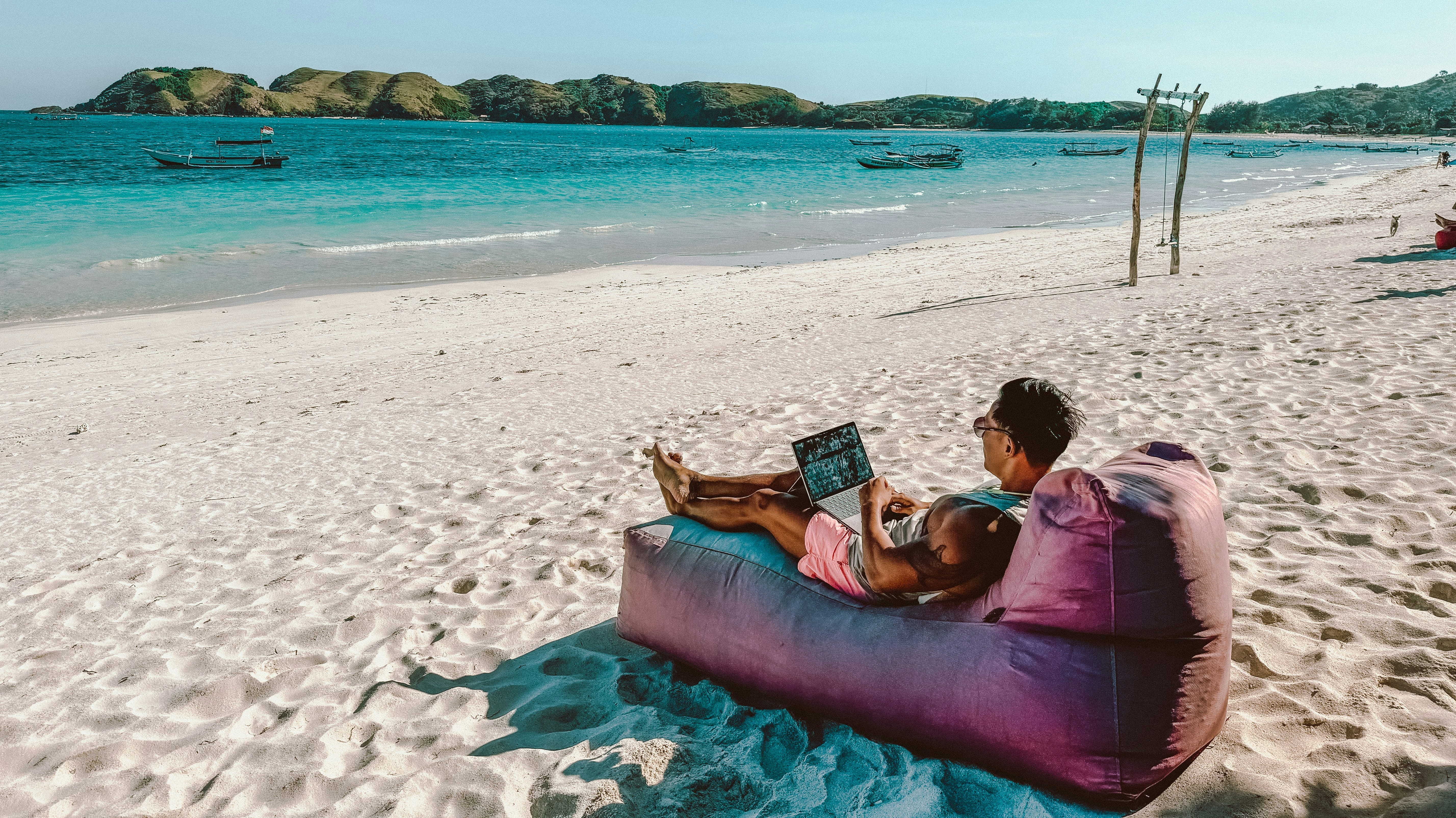 Person on beanbag using laptop on beach