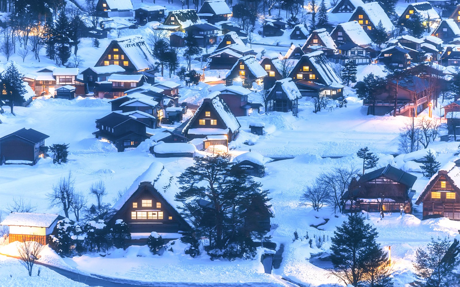 Traditional gassho-zukuri houses in snow-covered Shirakawa-go village, illuminated at dusk.