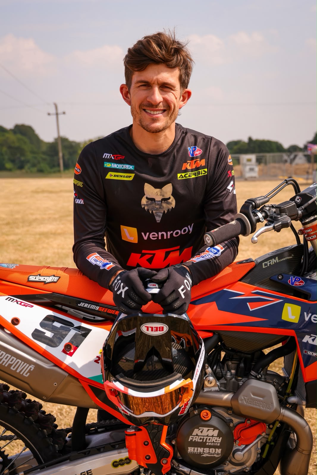 Jeremy Seewer smiling while leaning on his number 91 Van Venrooy KTM bike at an MXGP event