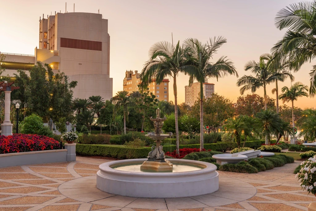 A serene park fountain surrounded by palm trees and modern buildings in the background, creating a tranquil urban oasis.