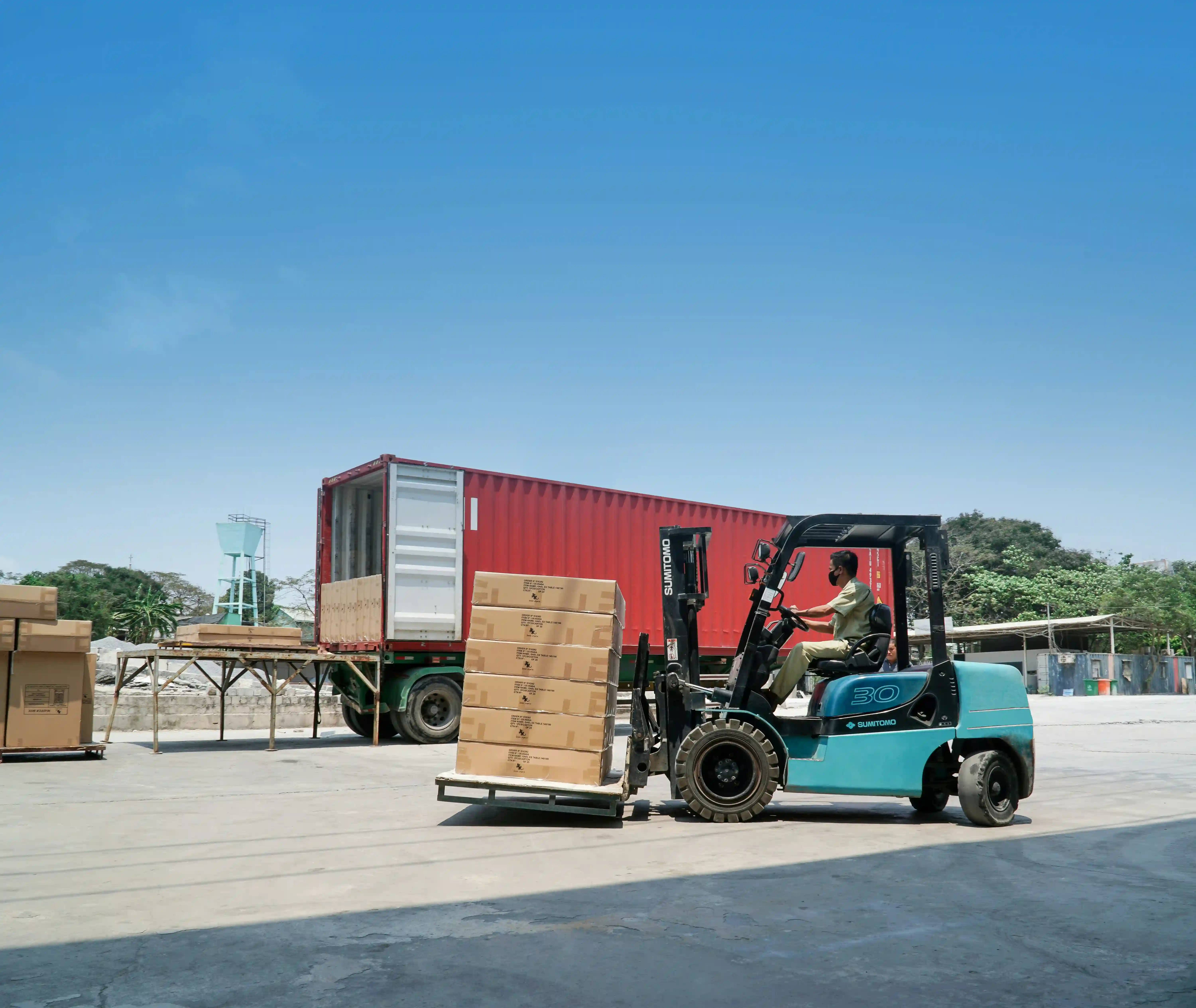 man on blue forklift truck unloads boxes from red container