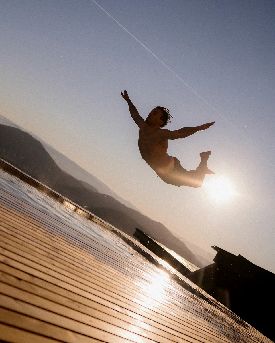 Person springt in der Abendsonne mit ausgebreiteten Armen kopfüber in den Pool