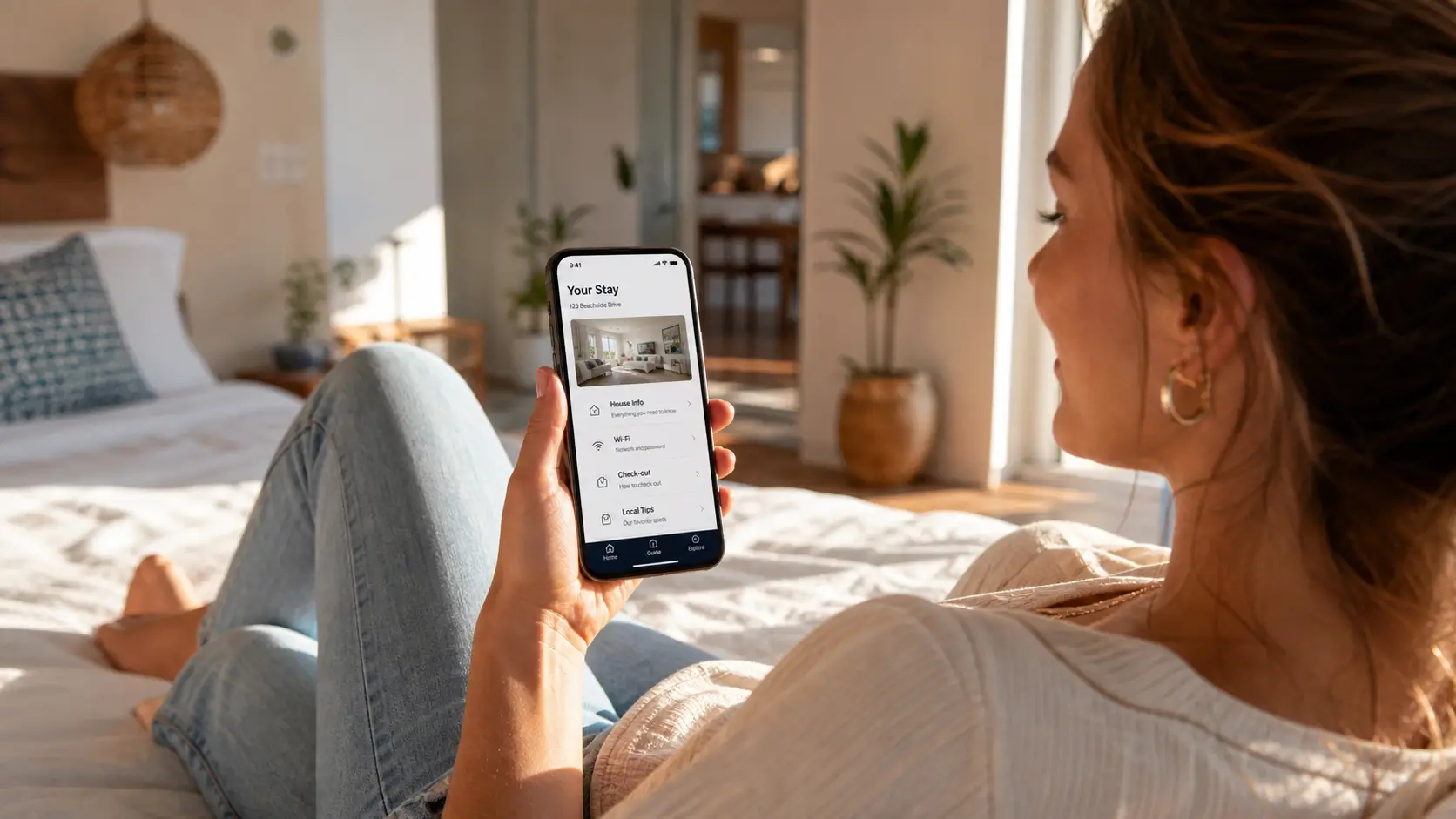 Guest holding a phone with a digital Airbnb guidebook open in a sunlit rental bedroom.