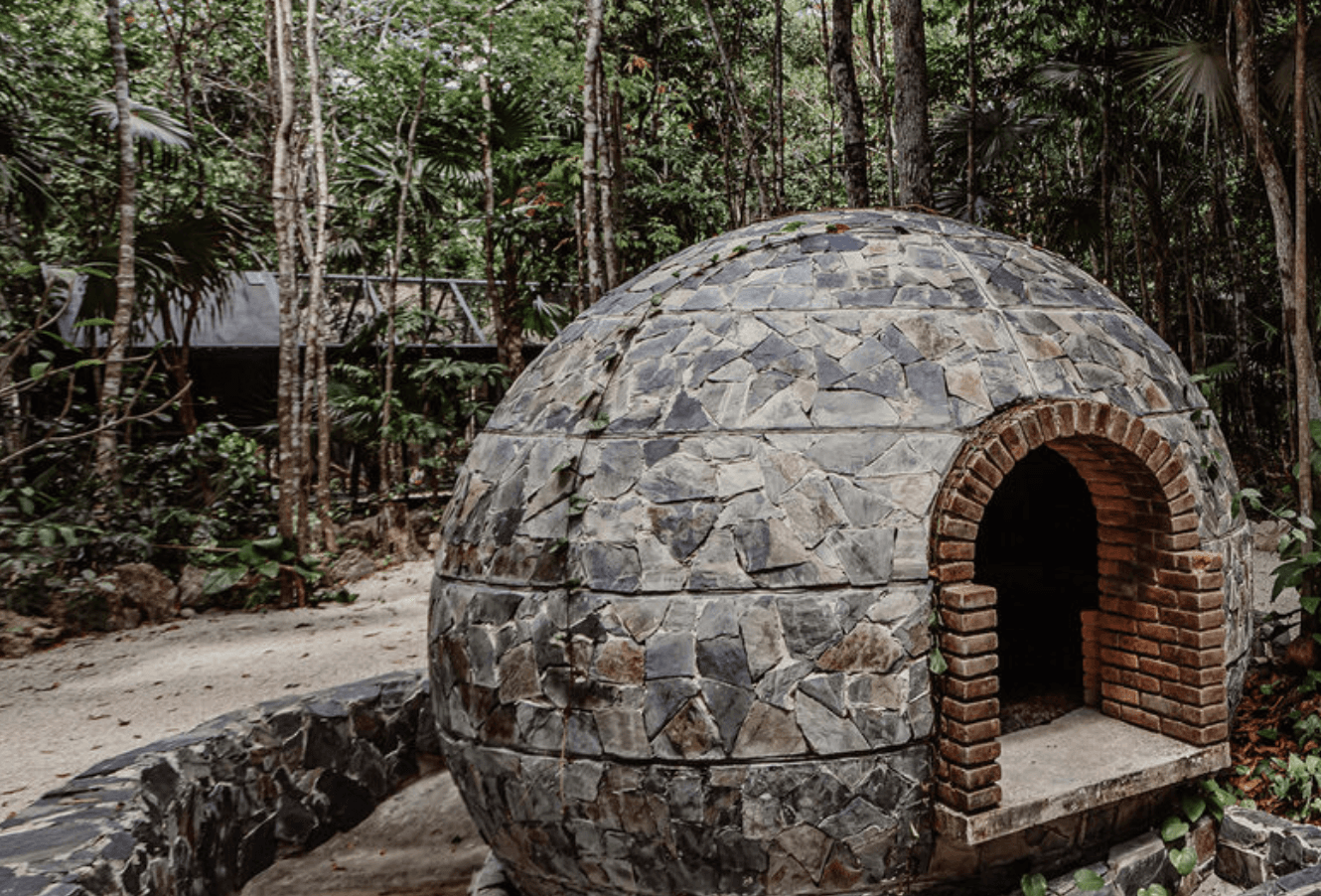 A person kneads fresh dough on a wooden kitchen counter dusted with flour, with pottery and a plant visible in the background, evoking a rustic baking atmosphere.