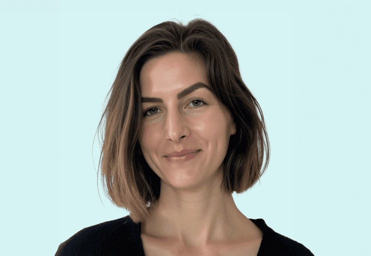 A person in a winter coat and furry hat walking along a snow-covered path through a forest of frosted trees.