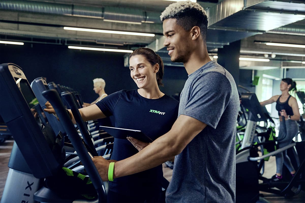 Ein XTRAFIT-Trainer gibt einem Mann Anweisungen an einem Trainingsgerät.