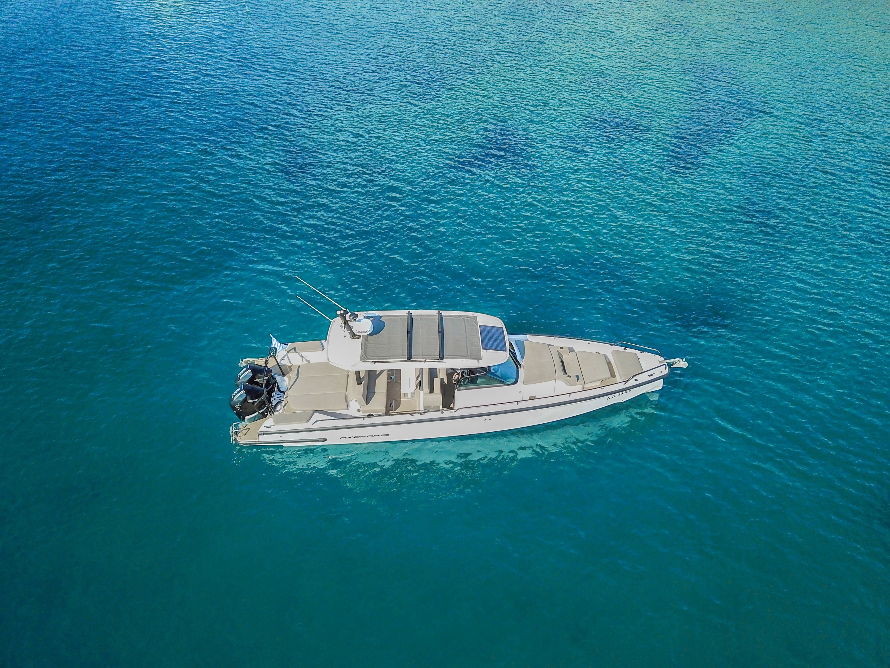 Aerial view of Axopar 37 Zeus motor yacht with white hull and twin outboard engines anchored in crystal-clear turquoise waters.