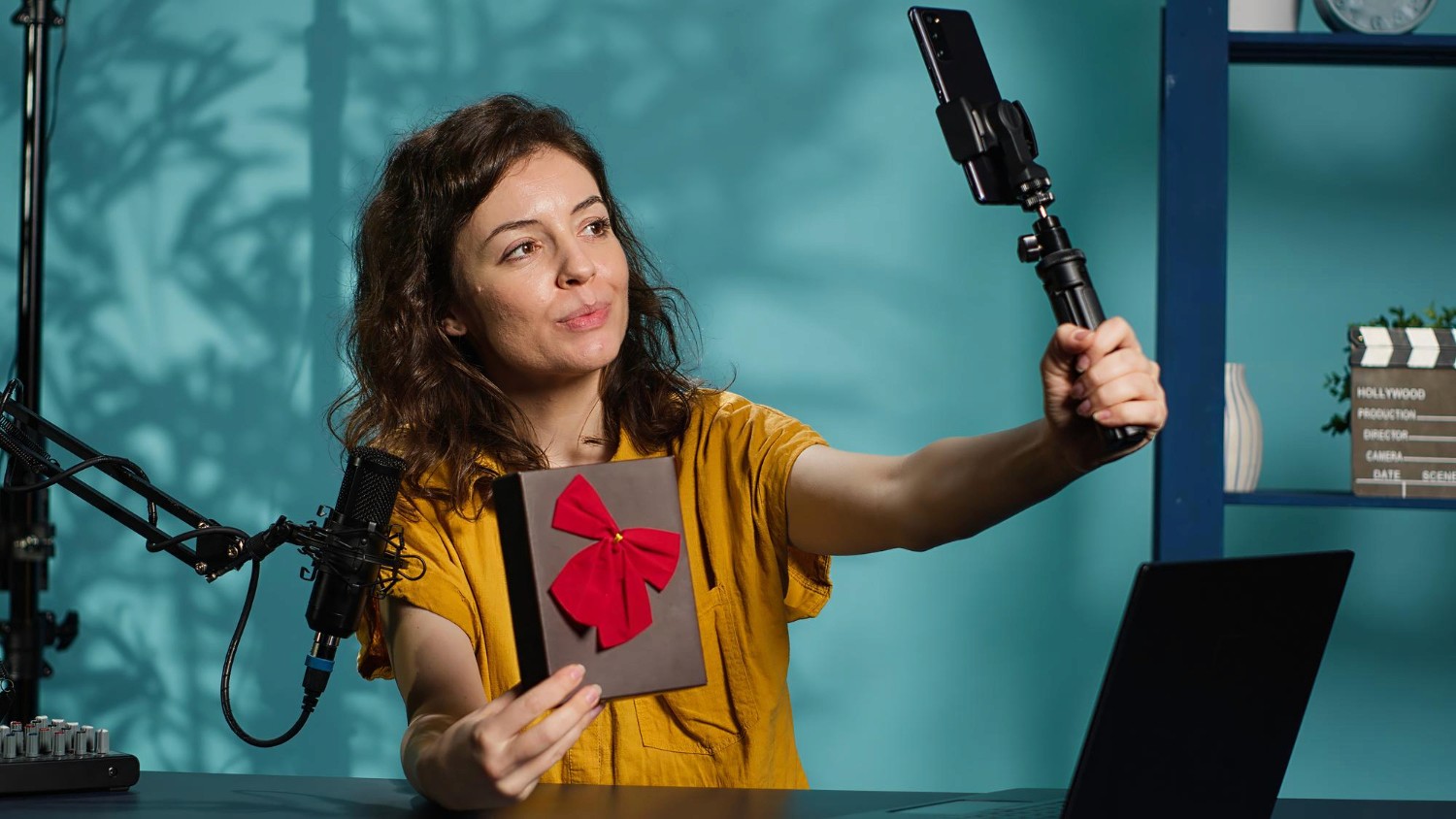 A woman confidently holds a gun in one hand and a wrapped gift in the other, showcasing a striking contrast.