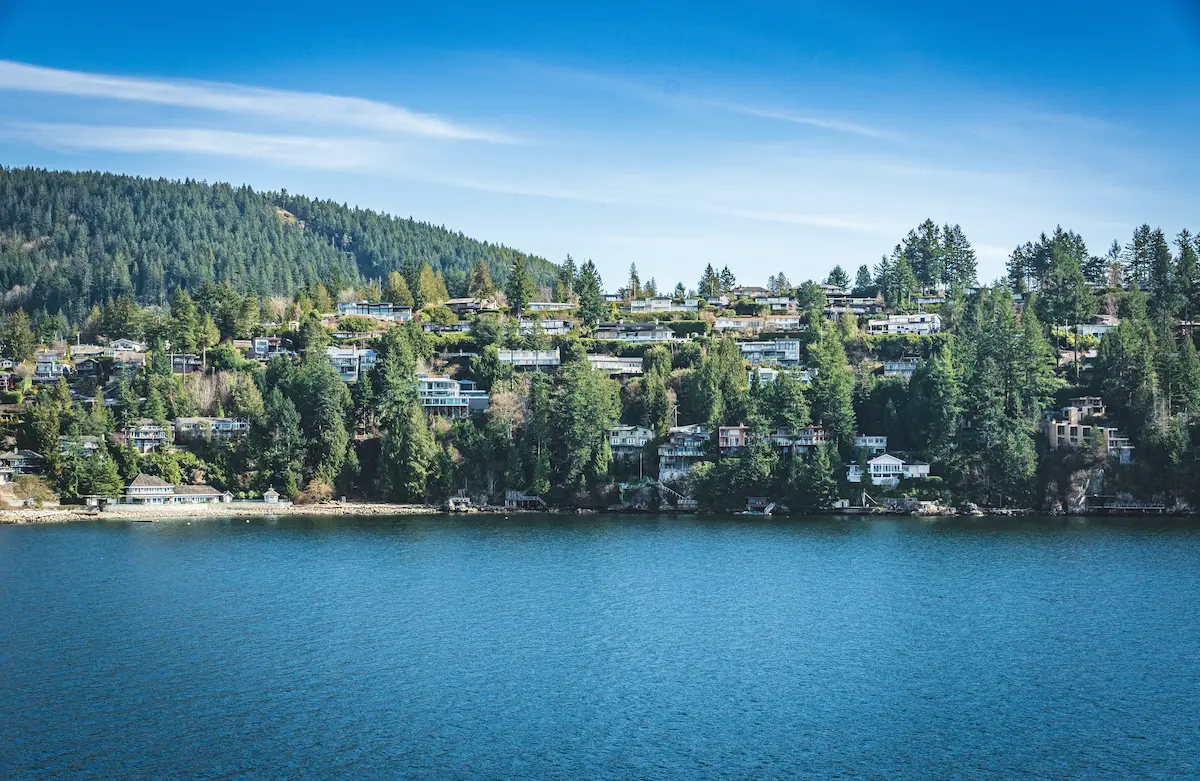 Waterfront view of West Vancouver with hillside homes surrounded by dense evergreen forest overlooking the blue ocean.